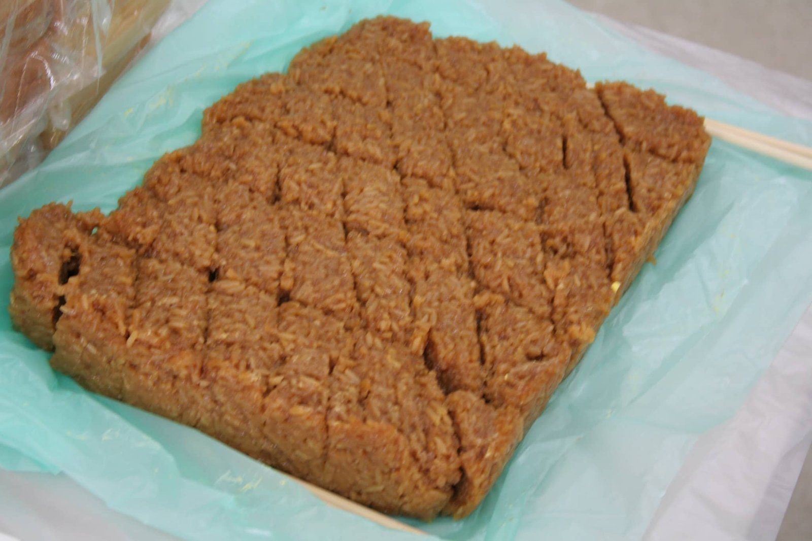 A traditional Filipino dessert called Biko, made of glutinous rice, coconut milk, and brown sugar. The sticky rice treat is neatly cut into squares and laid out on a plastic sheet, ready to be served.