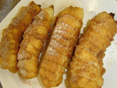 Four pieces of deep-fried banana skewers coated in caramelized sugar, placed on a white plate, with a dusting of cinnamon for added flavor.