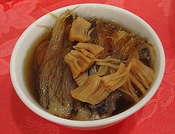 A small white bowl containing 'Buddha Jumps Over The Wall,' a traditional and luxurious Chinese soup. The dish features a rich broth with layers of intricate ingredients like mushrooms, bamboo shoots, and leafy greens. The soup is known for its complex flavors and premium components, symbolizing a feast of indulgence.