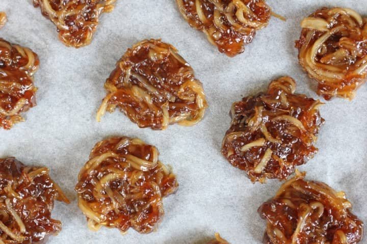 Several pieces of Bukayo, a Filipino delicacy made from caramelized coconut strips, arranged on a sheet of parchment paper. The Bukayo has a glossy, sticky texture with a rich brown color, showcasing its sweet and chewy nature.