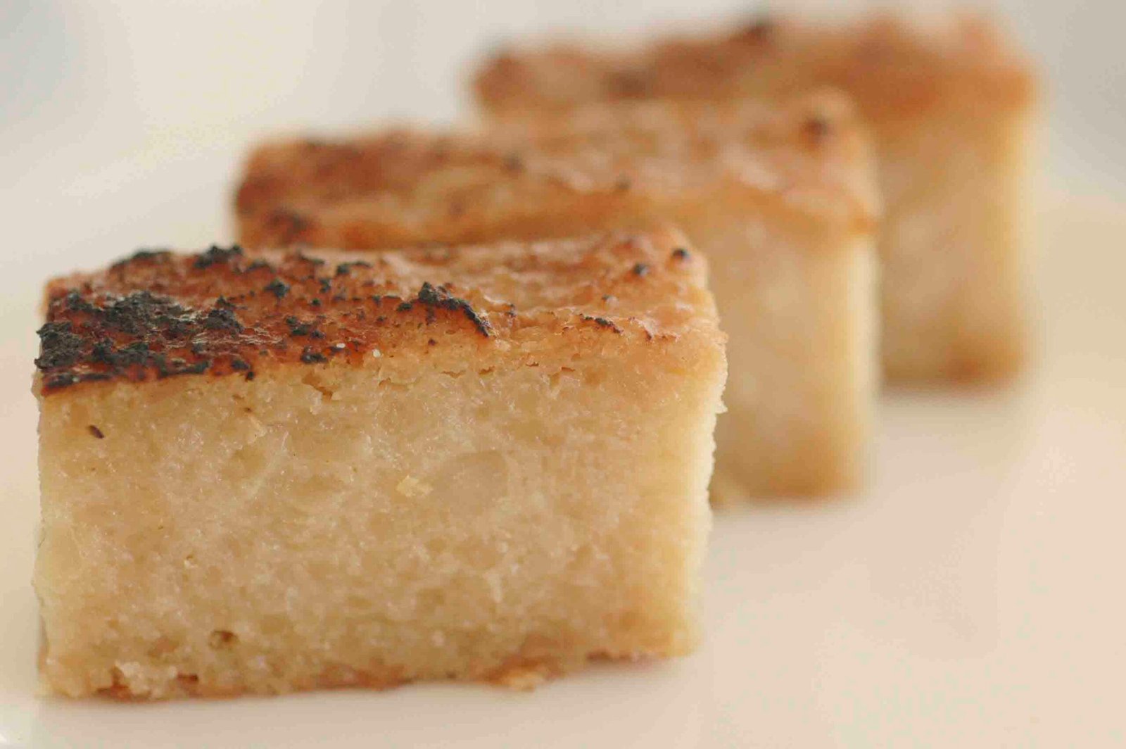 Three pieces of Cassava Pudding, each with a golden-brown crust and a dense, moist interior. The pudding has a slightly caramelized top, adding a rich texture and flavor to this traditional Filipino dessert.