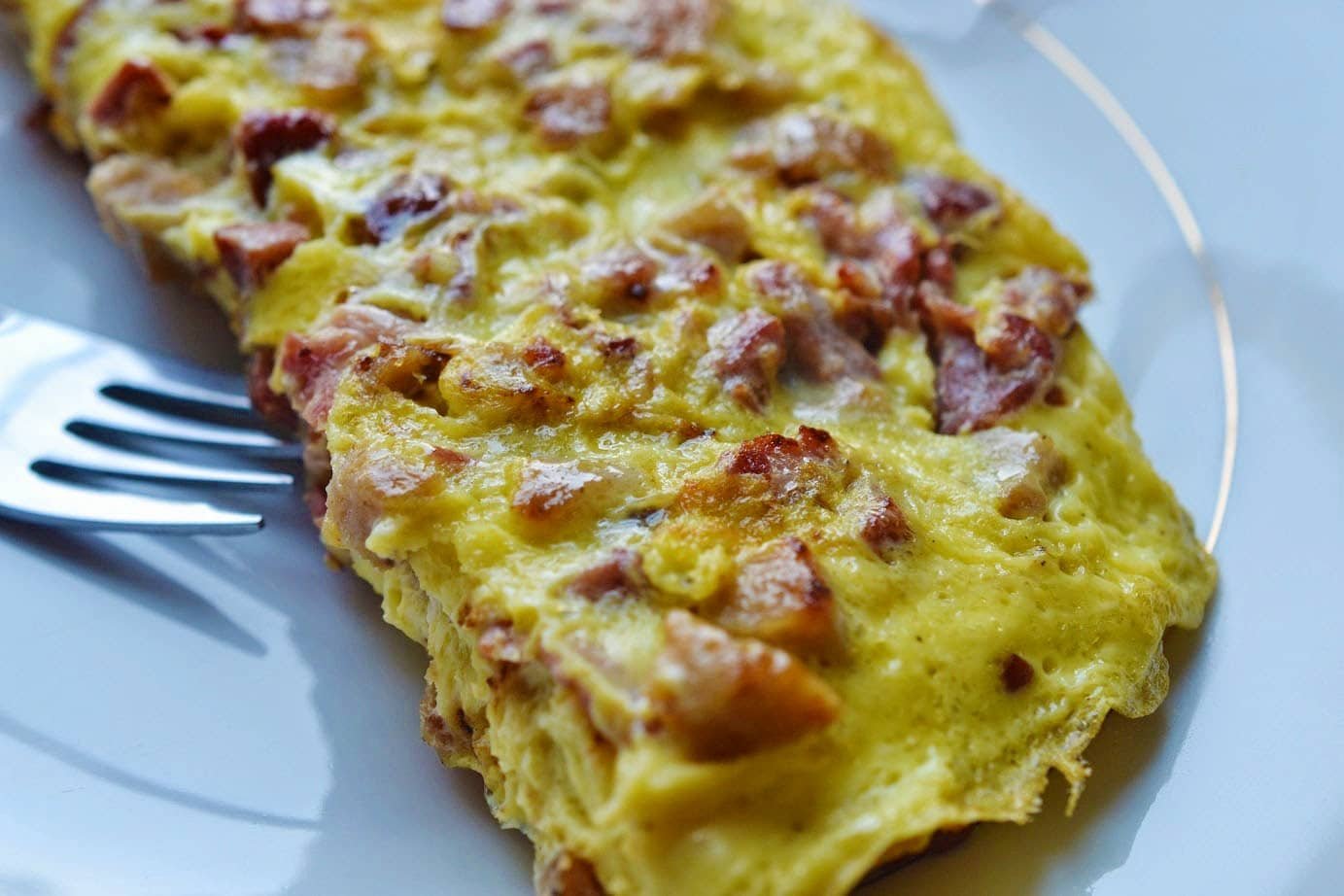 A close-up view of a golden, fluffy omelet filled with chunks of savory corned beef and melted cheese. The omelet has a crispy outer edge, and the cheese is oozing from within, giving it a rich and delicious texture.