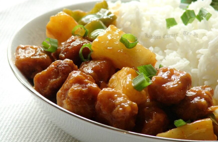 The image shows Chicken Adobo with Pineapple, a Filipino dish featuring tender chicken pieces cooked in a savory adobo sauce and garnished with chunks of pineapple. The dish is served alongside a portion of white rice and sprinkled with chopped green onions, adding a burst of color and freshness.