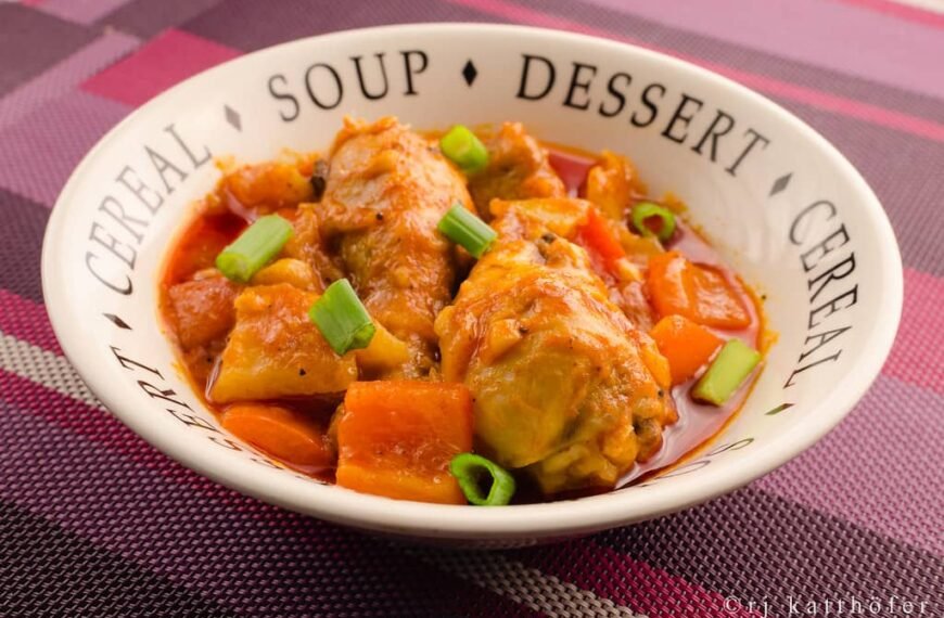 A bowl of Chicken Afritada with potatoes and carrots in a rich tomato sauce, garnished with green onions.