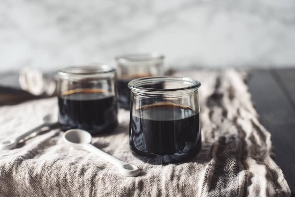 mall glass jars filled with rich coffee jelly, set on a textured cloth with white teaspoons nearby, perfect for a refreshing coffee jelly recipe.