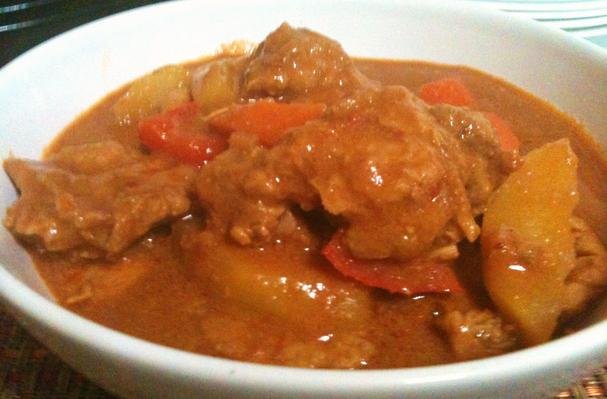 A bowl of Pork Caldereta, a rich and hearty Filipino stew. The dish features tender pork chunks in a thick, flavorful tomato-based sauce. Visible in the stew are potato wedges, carrots, and red bell peppers, all simmered together with the pork, creating a savory and slightly spicy flavor. The dish is known for its creamy, slightly sweet, and tangy sauce, commonly served with steamed rice.