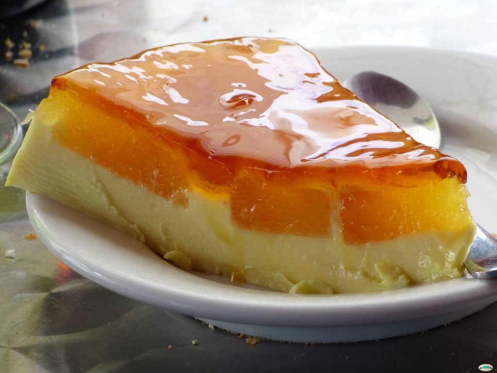 A slice of creamy cream cheese leche flan with a smooth caramel topping, served on a white plate, highlighting the rich layers and glossy finish—perfect for a cream cheese leche flan recipe.