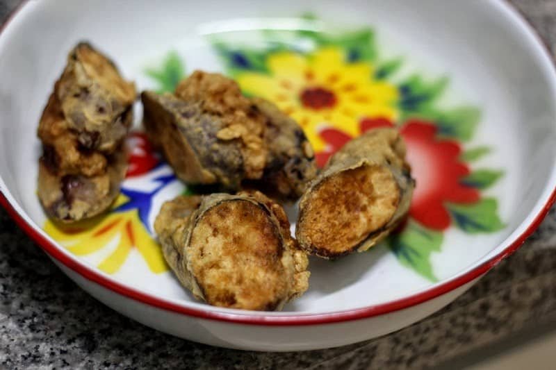 Several pieces of Crispy Eggplant served in a colorful floral-patterned bowl. The eggplant slices are coated in a golden, crunchy batter, offering a visually appealing and appetizing snack or side dish.