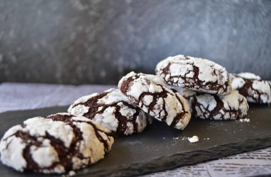 An arrangement of Dark Choco Crinkles Cookies on a slate serving board. The cookies are rich and chocolatey, with a soft, fudgy center and a crackled, powdered sugar coating that gives them a distinctive crinkled appearance, making them an indulgent treat for chocolate lovers.