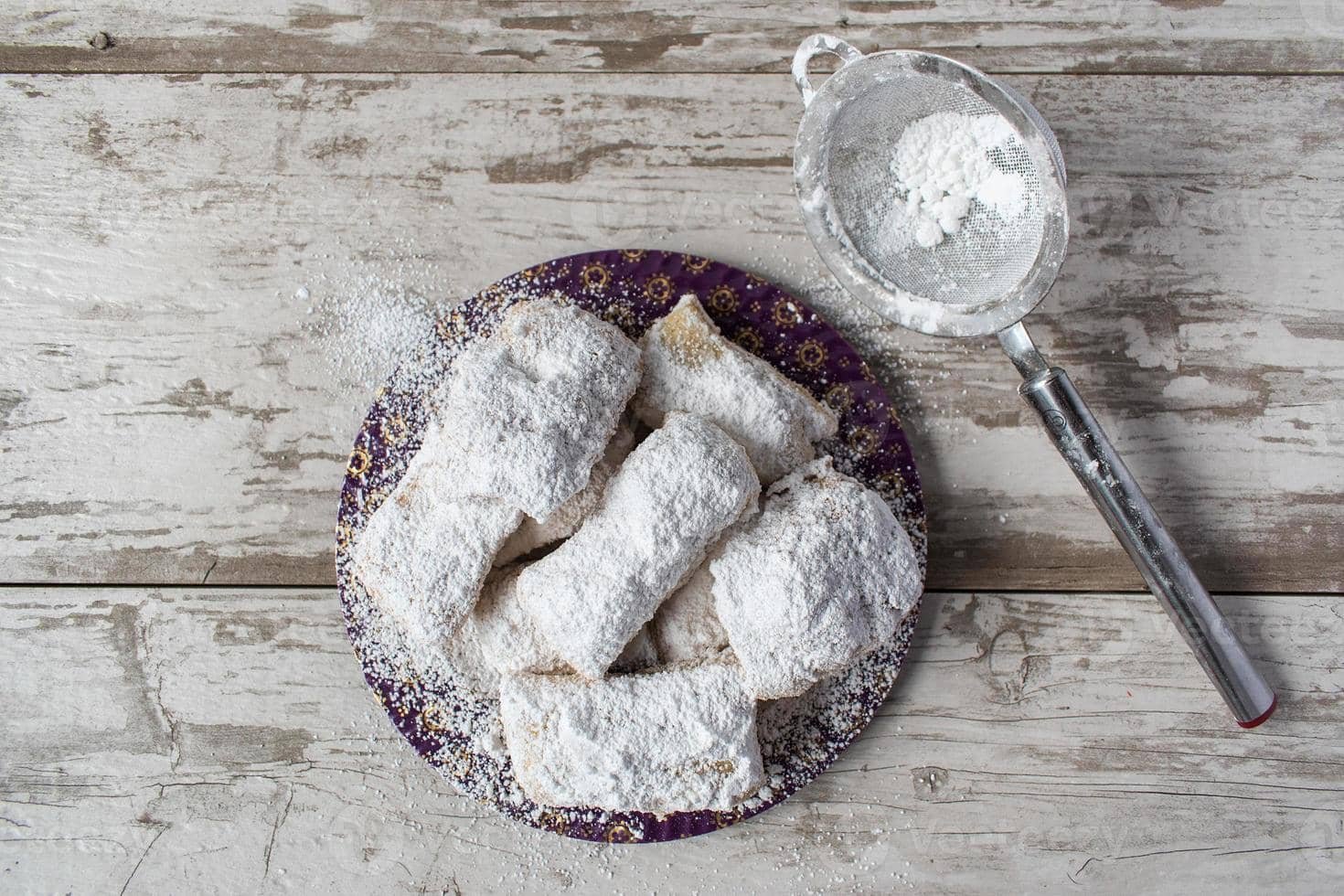 A plate of freshly made Espasol, a Filipino rice flour delicacy, generously dusted with powdered sugar. The rectangular treats are neatly arranged on a patterned plate, with a sieve beside them showing the remnants of sugar dusting.