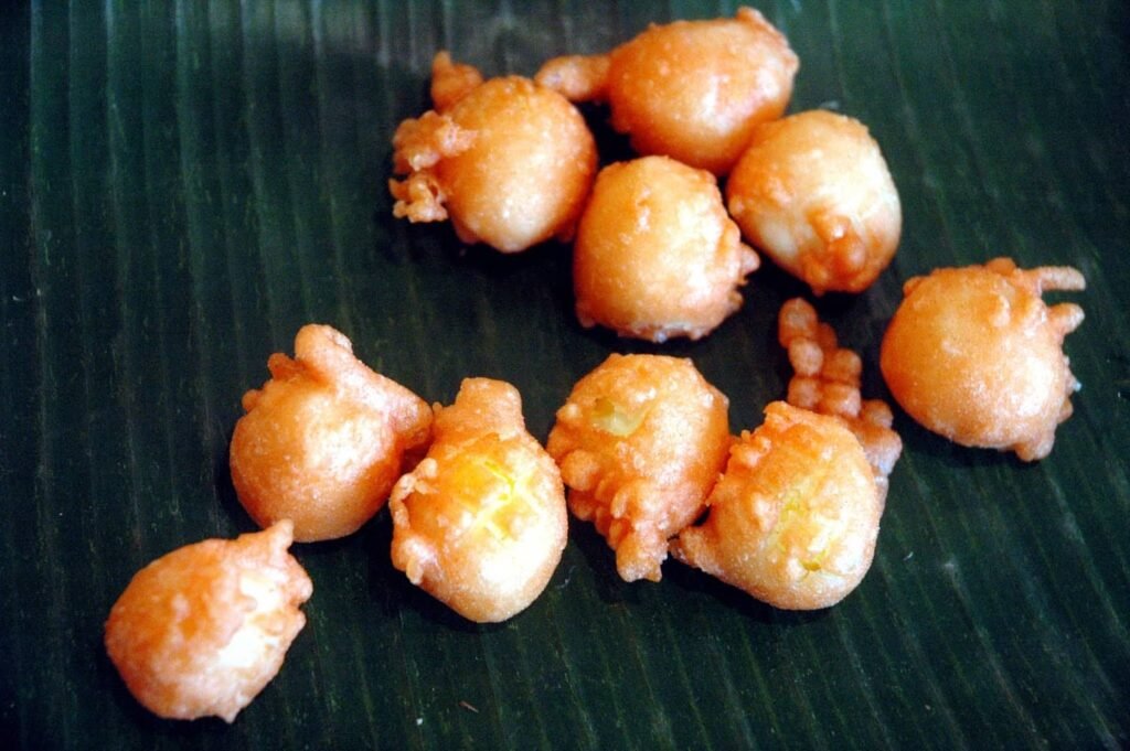 A serving of Easy Kwek-Kwek, featuring several pieces of quail eggs coated in a crispy, golden-orange batter. The bite-sized snacks are arranged on a banana leaf, showcasing their crunchy texture and vibrant color, making them an enticing Filipino street food.