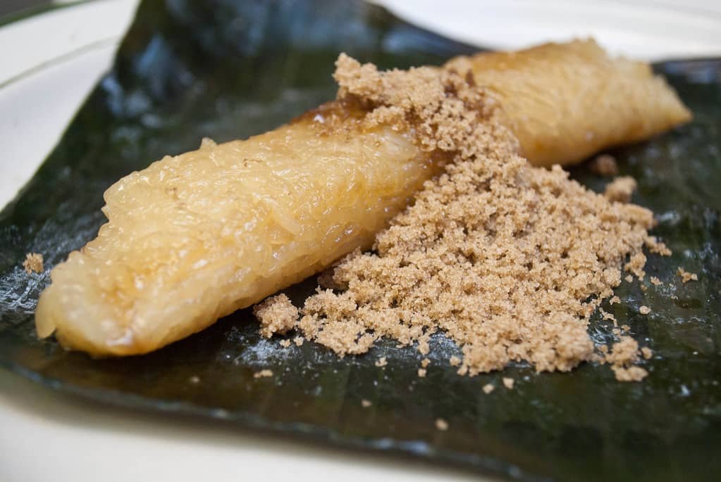 A piece of Suman sa Lihiya, a traditional Filipino sticky rice delicacy, served on a banana leaf and topped with a sprinkle of brown sugar. The suman has a glossy, chewy texture and is wrapped in a banana leaf to enhance its flavor, showcasing its simplicity and deliciousness.