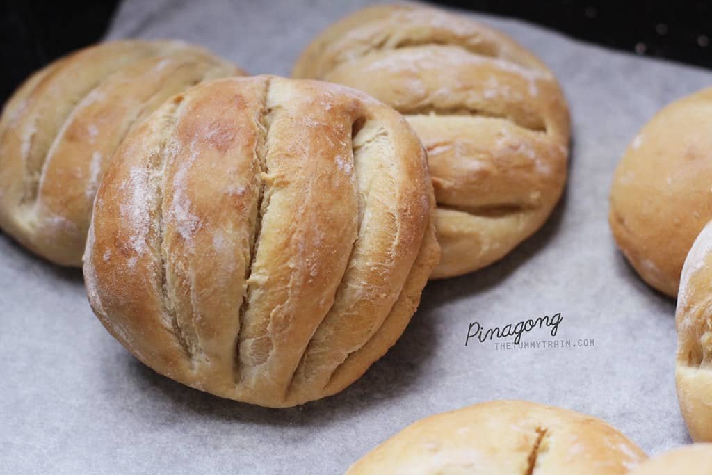 Freshly baked Filipino Monay bread, golden brown with a soft, dense texture, displayed on parchment paper, perfect for an easy and traditional Filipino Monay Bread recipe.