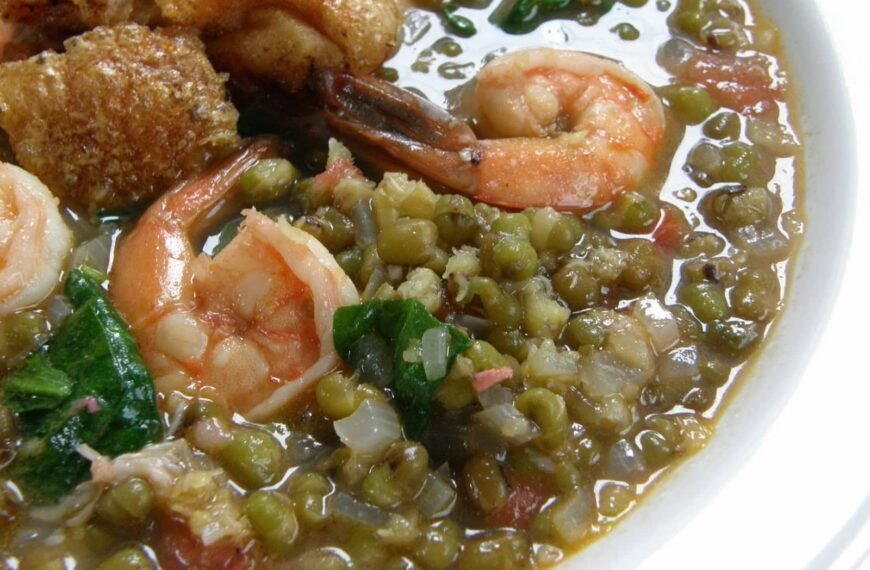 A close-up view of Ginataang Kangkong, a savory Filipino dish made with fresh shrimp, crispy pork, and mung beans in a coconut milk-based broth. The dish features water spinach (kangkong) adding a leafy texture to the mix.