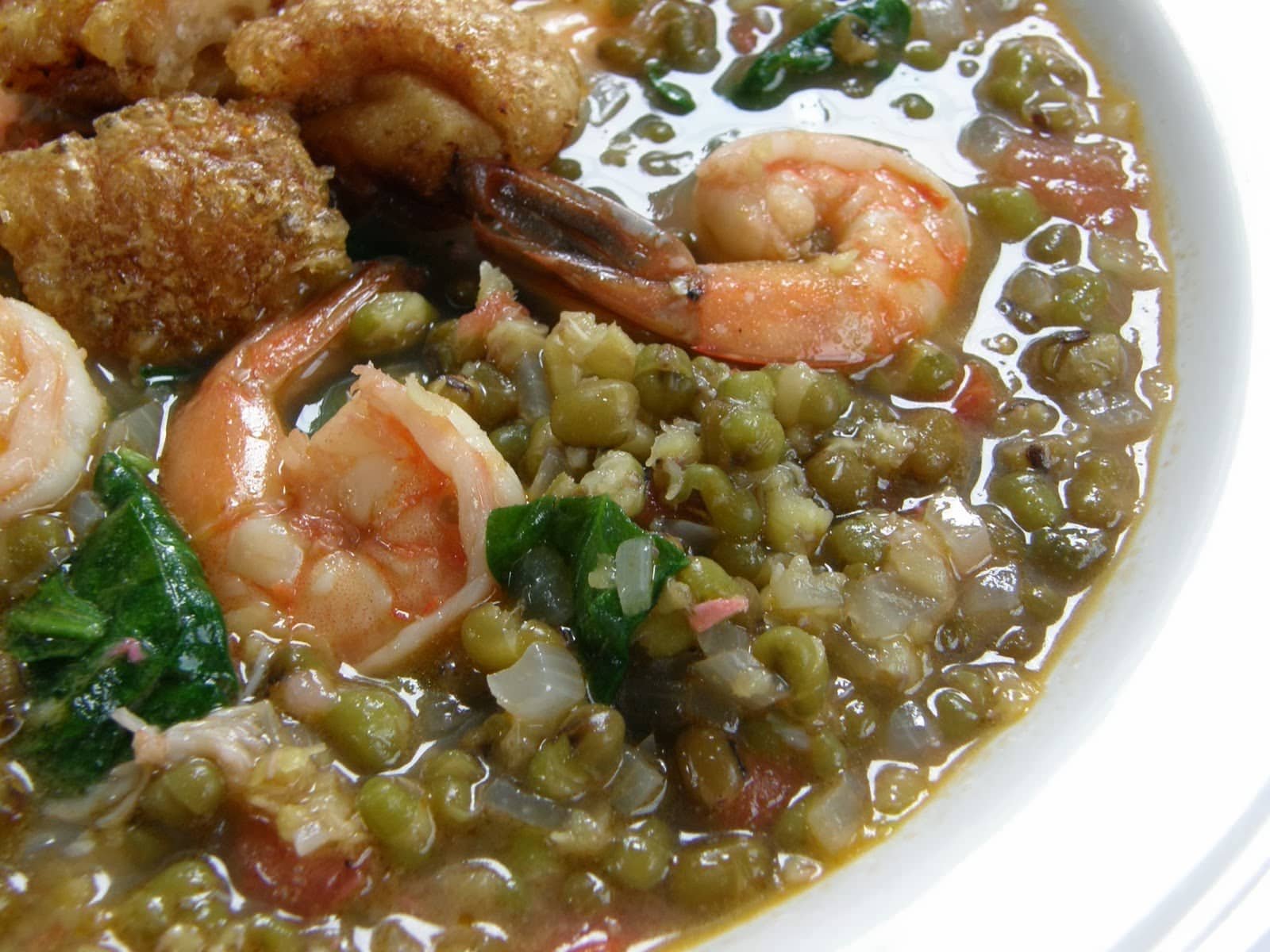 A close-up view of Ginataang Kangkong, a savory Filipino dish made with fresh shrimp, crispy pork, and mung beans in a coconut milk-based broth. The dish features water spinach (kangkong) adding a leafy texture to the mix.