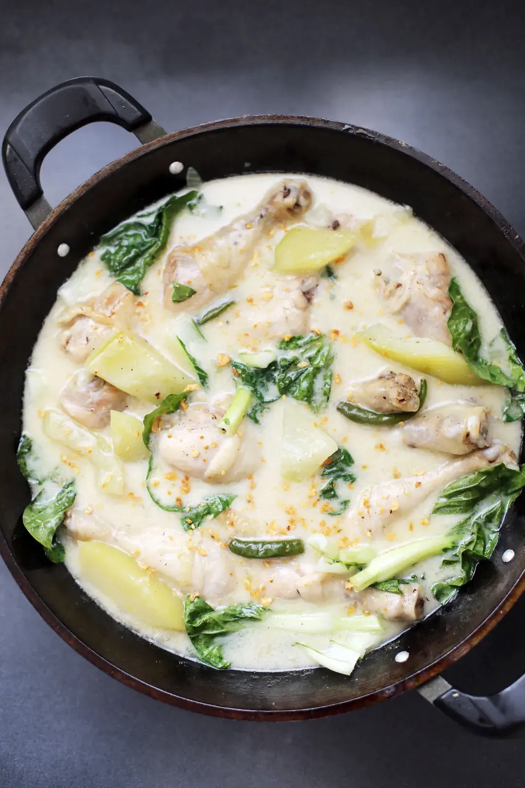 A pot of creamy Ginataang Papaya with chicken drumsticks, papaya slices, leafy greens, and a rich coconut milk broth, garnished with garlic bits.