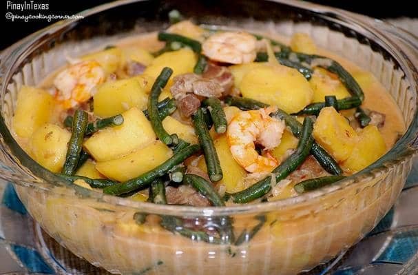 A colorful bowl of Ginataang Sitaw at Kalabasa, a traditional Filipino dish made with long green beans (sitaw), squash (kalabasa), shrimp, and pork. The ingredients are simmered in a rich and creamy coconut milk broth, creating a comforting and flavorful dish.