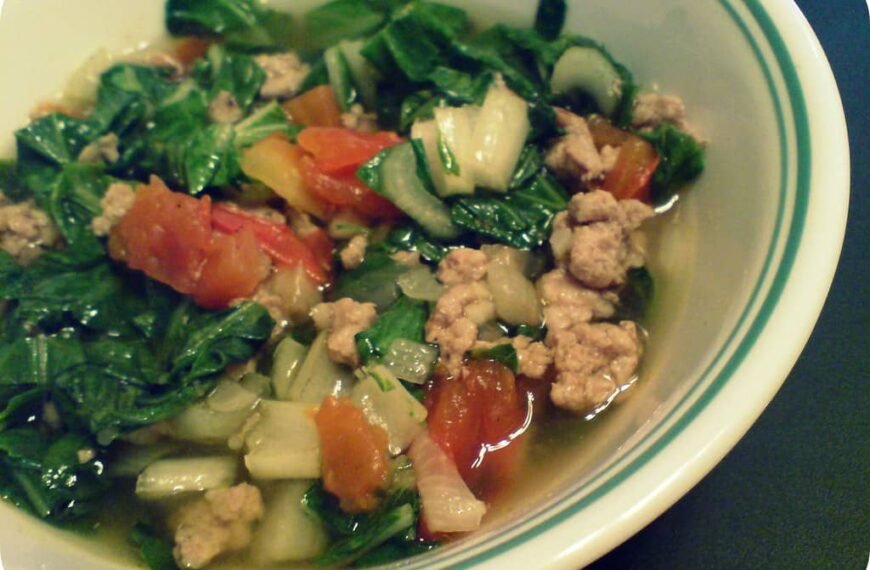 A bowl of Giniling na Menudo, a Filipino dish featuring sautéed ground pork with vegetables. The dish includes chopped green leafy vegetables, diced tomatoes, and bits of cooked pork in a flavorful broth. The vibrant greens and reds from the vegetables complement the tender pork, creating a hearty and nourishing dish commonly enjoyed with rice.