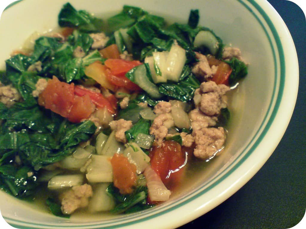 A bowl of Giniling na Menudo, a Filipino dish featuring sautéed ground pork with vegetables. The dish includes chopped green leafy vegetables, diced tomatoes, and bits of cooked pork in a flavorful broth. The vibrant greens and reds from the vegetables complement the tender pork, creating a hearty and nourishing dish commonly enjoyed with rice.