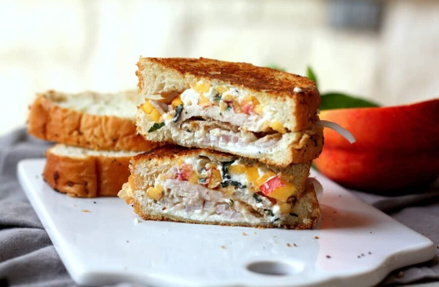 A grilled cheese sandwich with vegetables and cheese, cut in half and stacked on a cutting board.