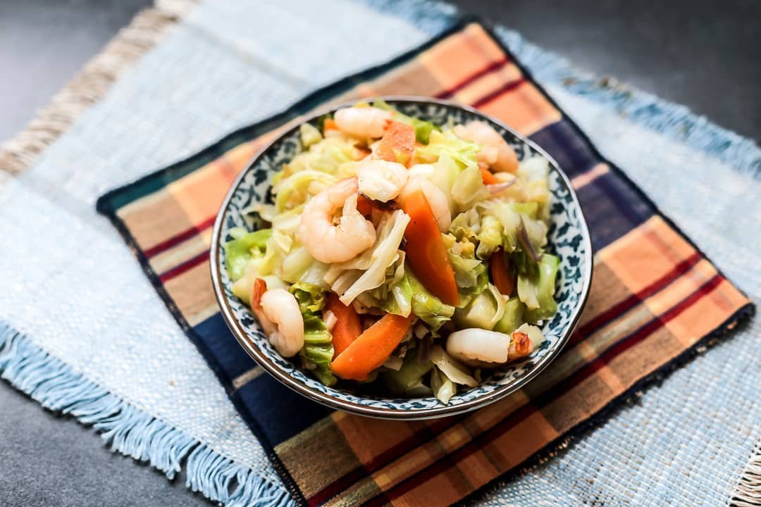 A vibrant dish of Hipon na may Repolyo, featuring fresh shrimp sautéed with crisp cabbage, carrots, and other vegetables. The dish is beautifully presented in a patterned bowl on a colorful woven mat, capturing the essence of a Filipino home-cooked meal. The vegetables and shrimp are cooked to perfection, with a balance of textures and flavors that make this dish both healthy and delicious.