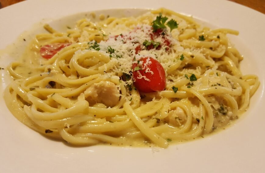 The image shows a plate of homemade carbonara, featuring creamy linguine pasta with cherry tomatoes, grated cheese, and garnished with fresh parsley. The sauce looks rich and cheesy, making for a delicious and comforting meal.