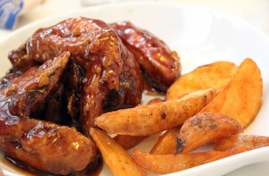 Honey garlic wings served with crispy potato wedges on a white plate.