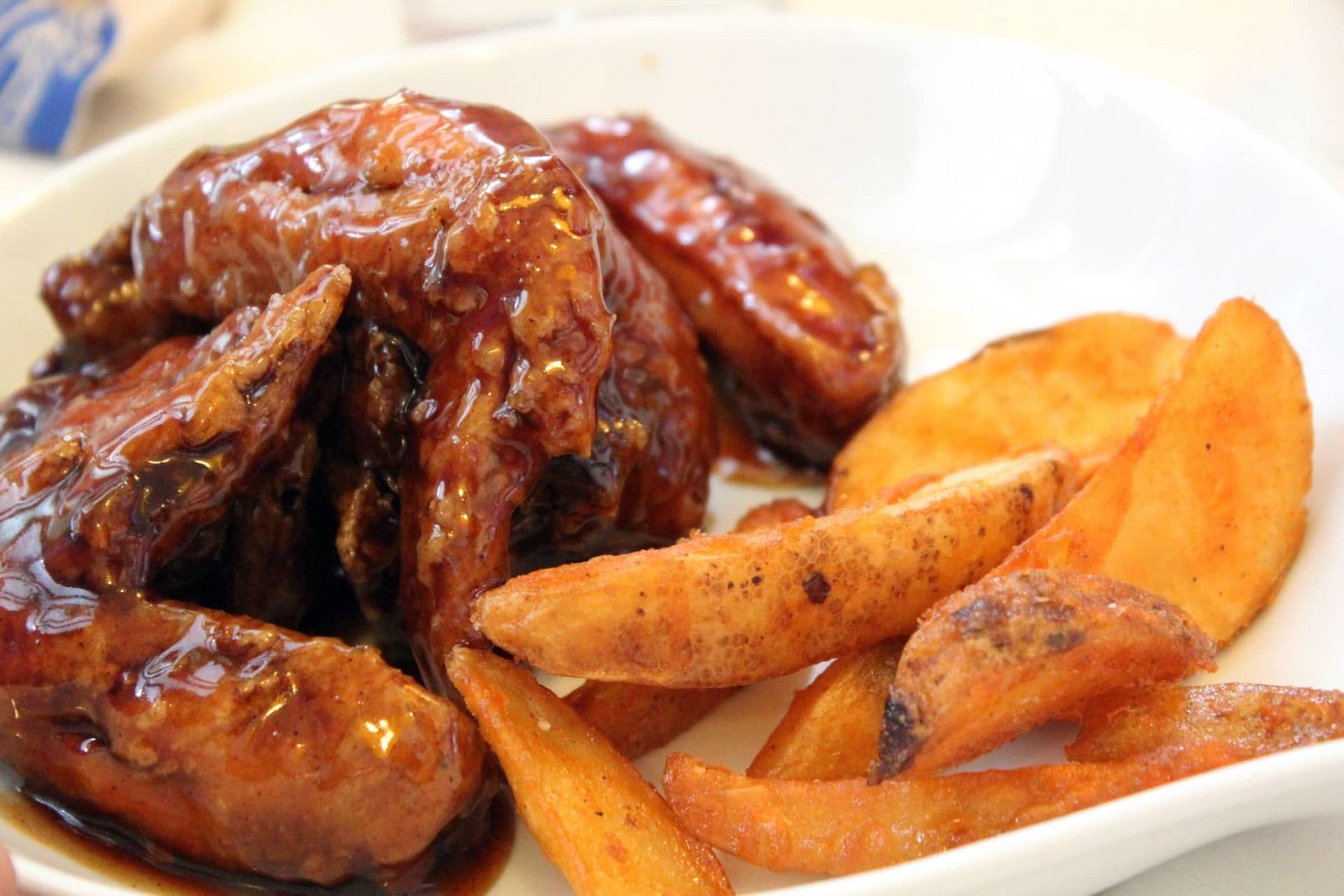Honey garlic wings served with crispy potato wedges on a white plate.