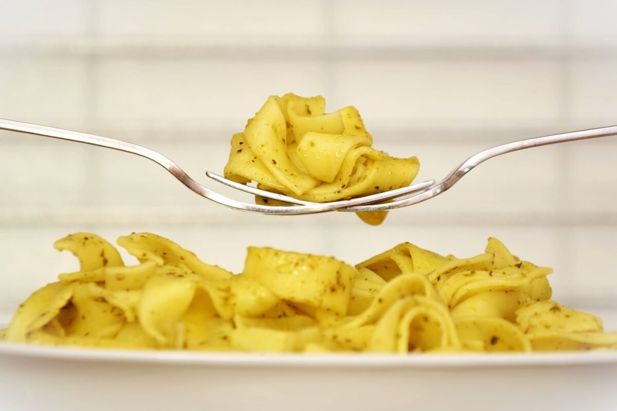 The image depicts a plate of creamy pasta, delicately lifted by a fork. The noodles are seasoned with herbs, showcasing the smooth texture and appealing yellow hue of a freshly prepared carbonara dish.