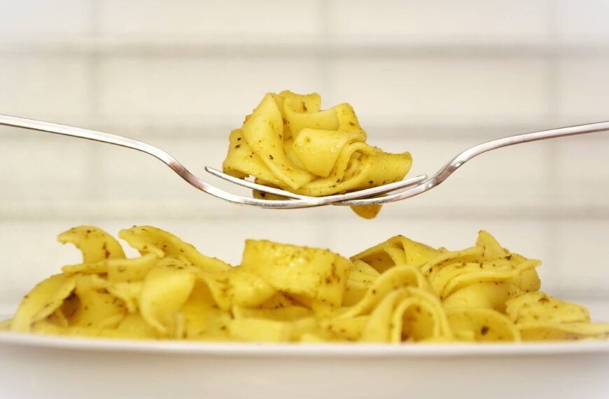 The image depicts a plate of creamy pasta, delicately lifted by a fork. The noodles are seasoned with herbs, showcasing the smooth texture and appealing yellow hue of a freshly prepared carbonara dish.