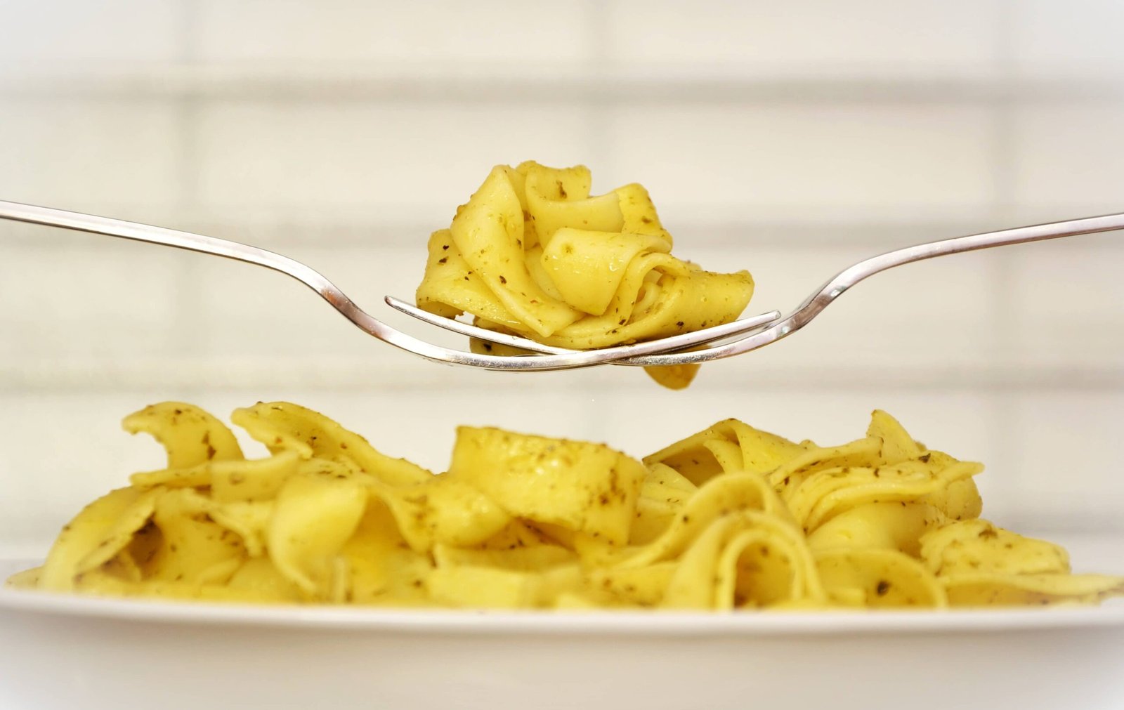 The image depicts a plate of creamy pasta, delicately lifted by a fork. The noodles are seasoned with herbs, showcasing the smooth texture and appealing yellow hue of a freshly prepared carbonara dish.