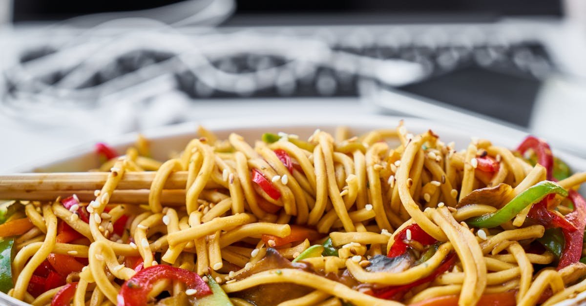 A bowl of stir-fried noodles with vegetables and sesame seeds.
