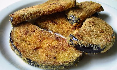 Crispy slices of Eggplant Steak, coated in a golden-brown breading, arranged on a white plate. The eggplant is cooked to perfection, with a crunchy exterior and tender inside, showcasing a delicious plant-based alternative to traditional steak.