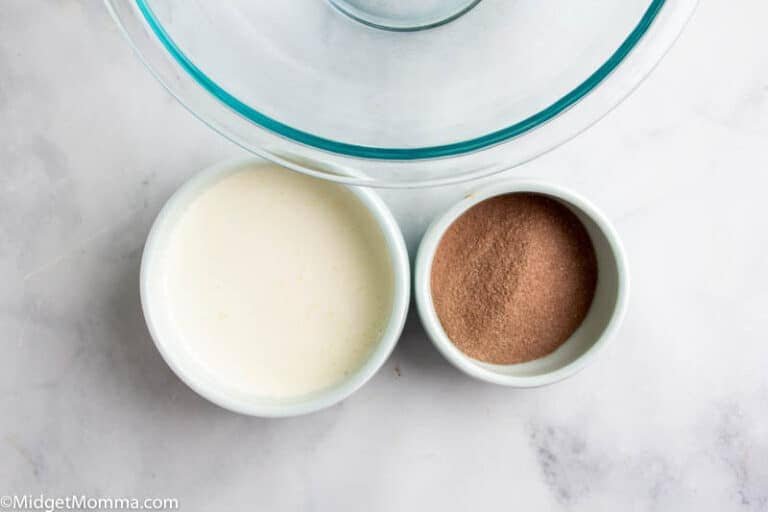 Ingredients for Milo Dalgona, featuring a bowl of whipped egg whites and sugar, and a small dish of Milo powder, prepared on a marble surface.