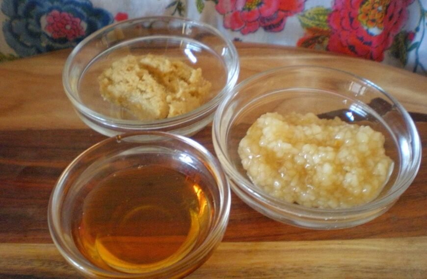 The image shows three small glass bowls containing ingredients for making sweet and sour sauce. One bowl holds minced ginger, another holds minced garlic in oil, and the last bowl contains a light, translucent liquid, possibly vinegar or oil.