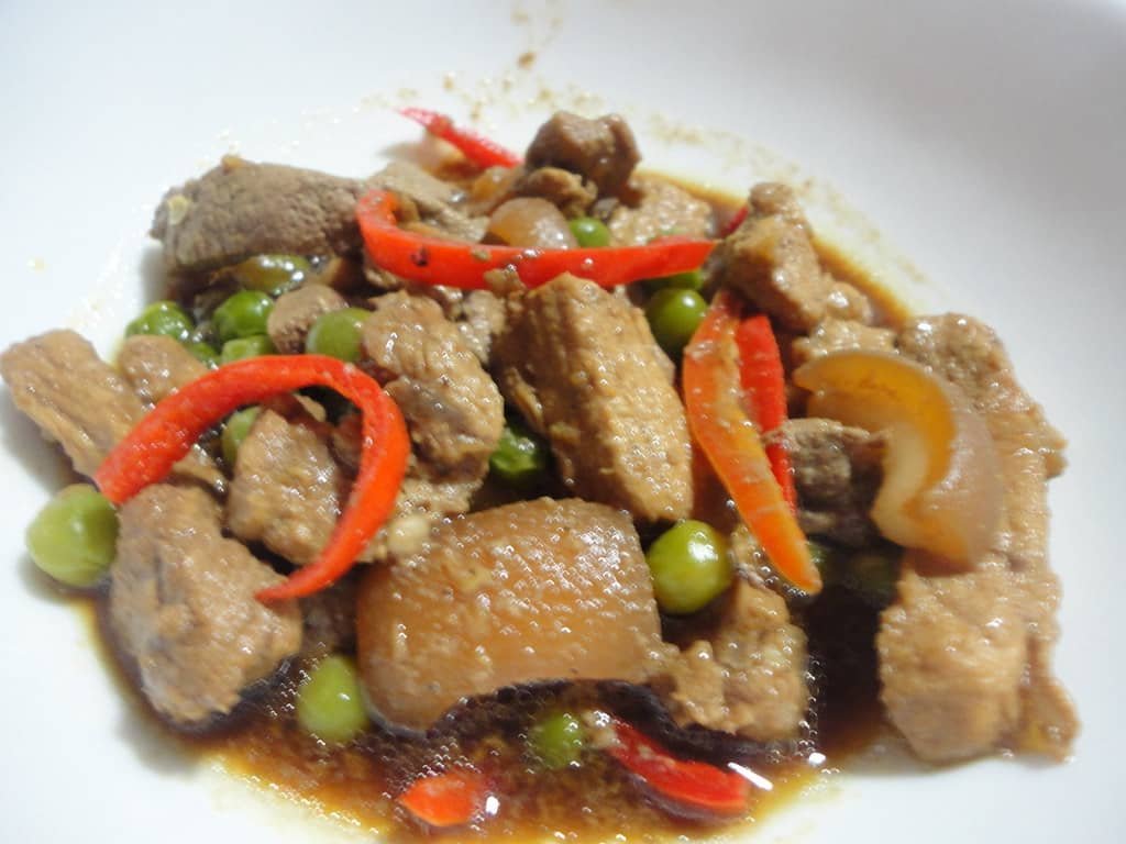 A serving of Igado, a traditional Filipino dish made with pork liver, kidneys, and meat, garnished with green peas and sliced red bell peppers in a savory sauce.