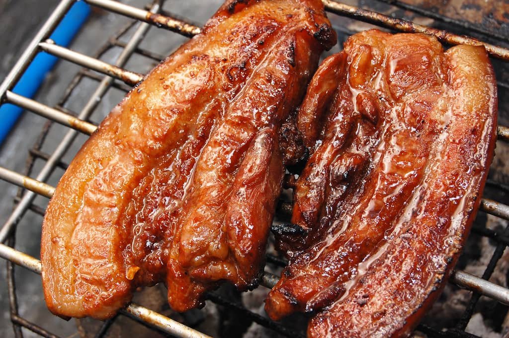 A close-up of two pieces of perfectly grilled pork belly (Inihaw na Liempo), glistening with caramelized marinade and beautifully charred, showcasing the classic Filipino recipe for smoky and tender pork barbecue.