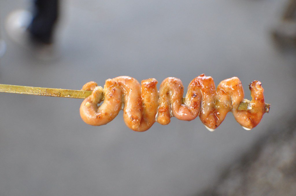 The image shows Isaw, a popular Filipino street food made from grilled chicken intestines, skewered and cooked over an open flame. The intestines are typically marinated in a flavorful sauce before grilling, resulting in a smoky, savory treat.