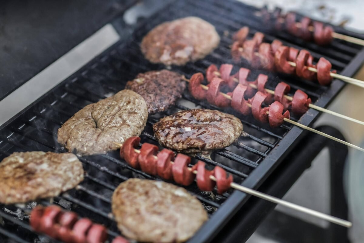 Burger patties and hotdog skewers grilling on a barbecue.