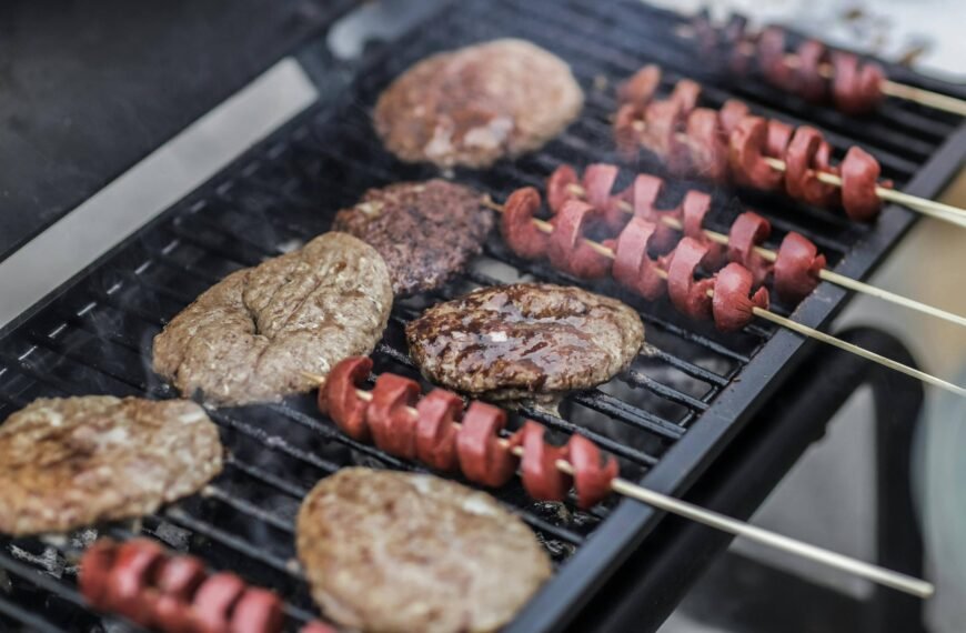 Burger patties and hotdog skewers grilling on a barbecue.