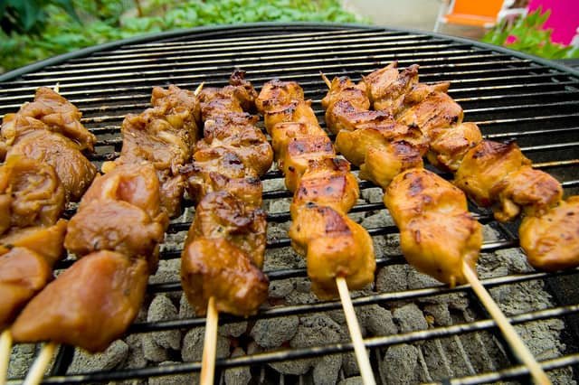 Skewers of marinated pork barbecue grilling over hot coals. The pork pieces are golden brown with slight charring, showcasing their juicy and flavorful texture, a popular Filipino street food delicacy.