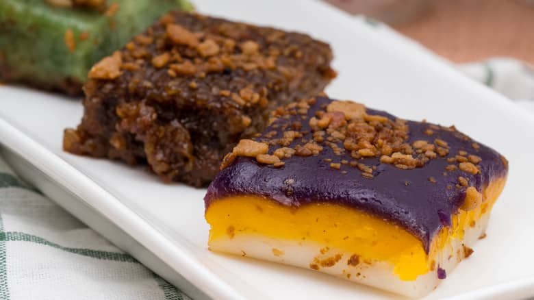 A close-up of two slices of traditional Filipino kakanin from Luzon, featuring vibrant layers of rice cakes with different colors and textures, topped with crunchy latik (coconut curds).