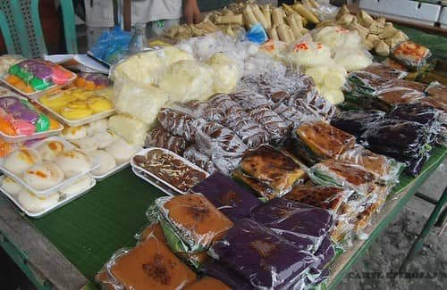 A variety of traditional Kakanin, or Filipino rice cakes, displayed at a market in the Visayas region, with different types of wrapped and colorful sweet treats arranged on a table.