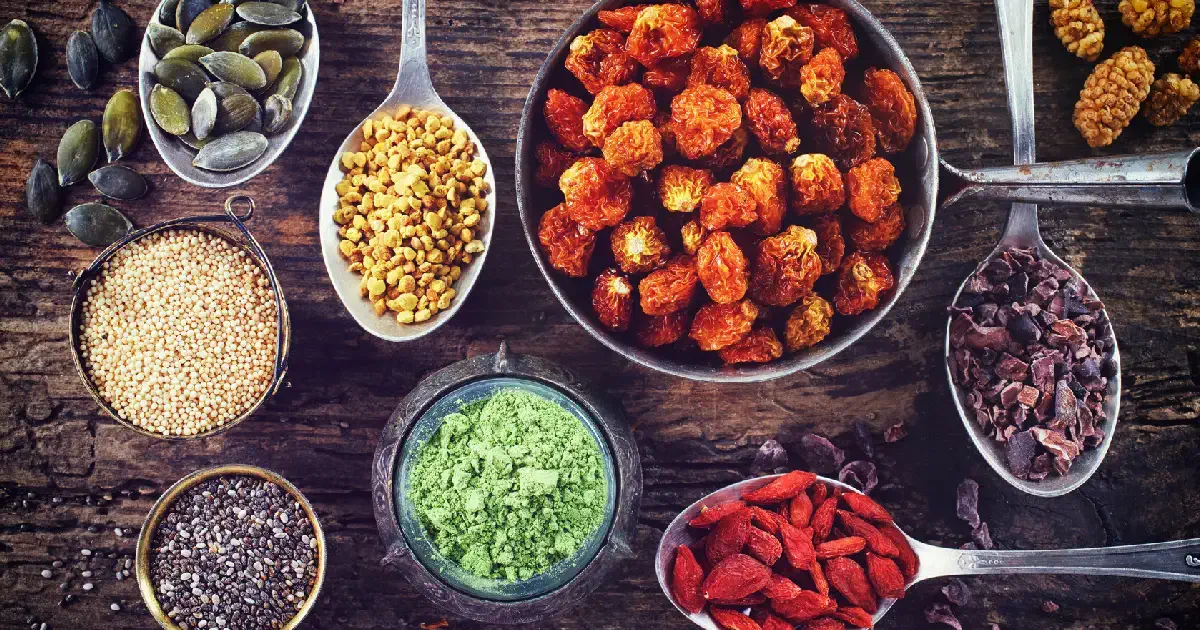 Assorted healthy seeds, nuts, and dried fruits displayed on spoons and bowls, representing foods to avoid to protect from arthritis pain.