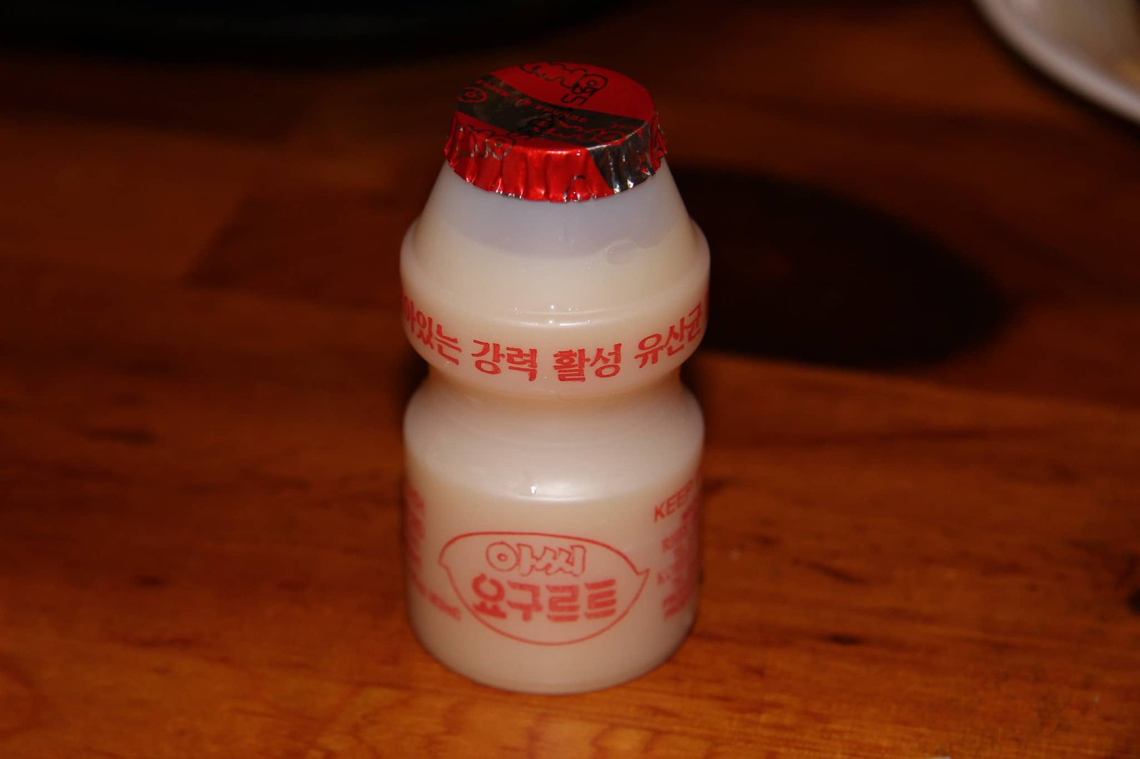 A single bottle of Yakult, a popular probiotic drink, placed on a wooden surface, with a red foil cap and Korean text on the label.