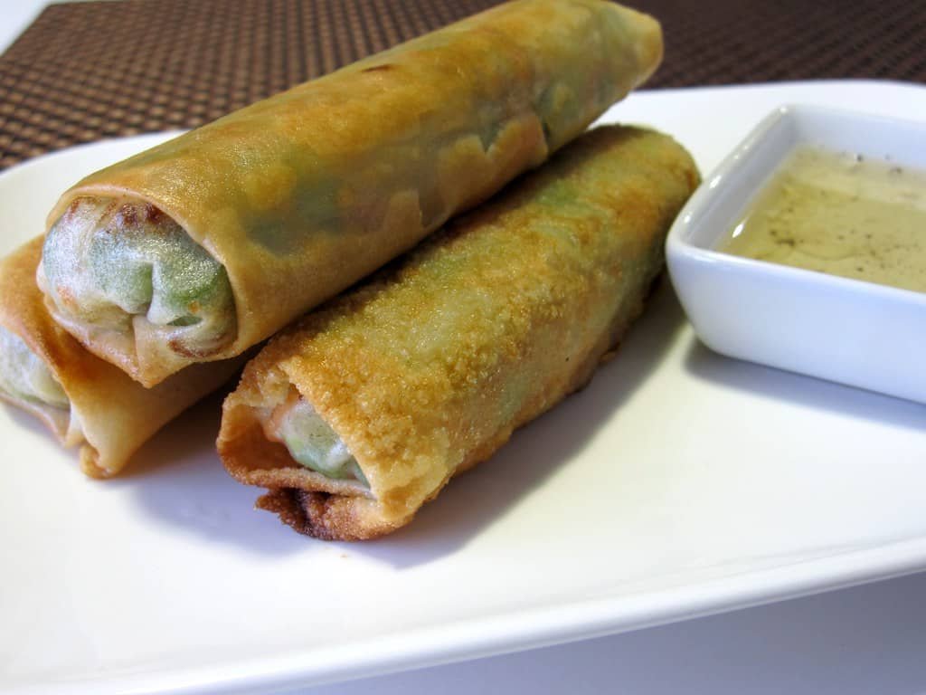 Golden brown Lumpiang Gulay (vegetable spring rolls) served on a white plate with a dipping sauce on the side. These crispy spring rolls are filled with fresh, sautéed vegetables, showcasing a delicious and healthy Filipino dish.