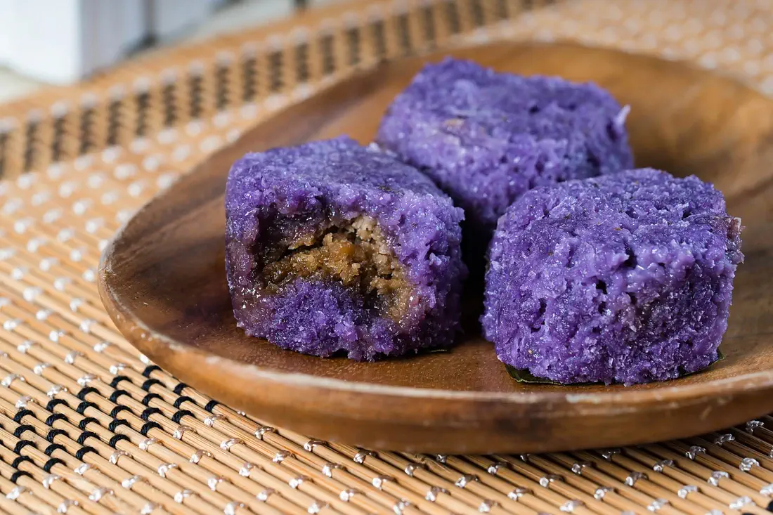 Three pieces of vibrant purple Maja De Ube, a Filipino dessert made from ube (purple yam), with a soft and chewy texture, served on a wooden plate—perfect for an authentic Maja De Ube recipe.