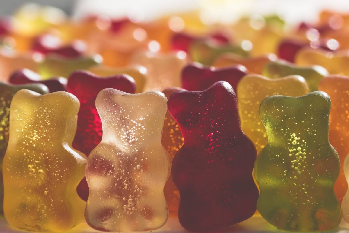 The image shows an assortment of colorful gummy bears in various translucent shades of red, yellow, green, and orange, with tiny bubbles visible within them, creating a vibrant and playful display.