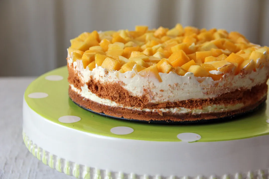 A delicious Mango Grahams Frozen Cake with layers of graham crackers, creamy filling, and topped with fresh mango chunks, displayed on a decorative cake stand.