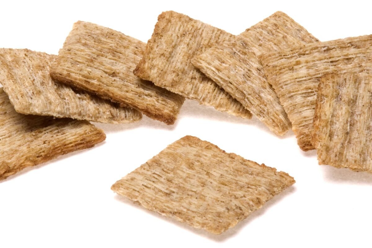A pile of square wheat crackers spread on a white surface.